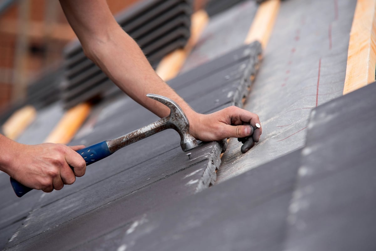 Skilled contractor hands carefully placing roofing tiles on a sloped building surface