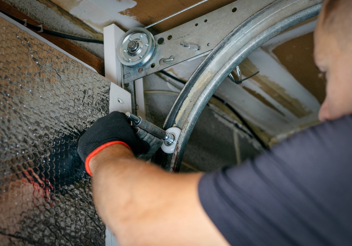 Contractor attentively repairing a garage door with tools, demonstrating focus and craftsmanship