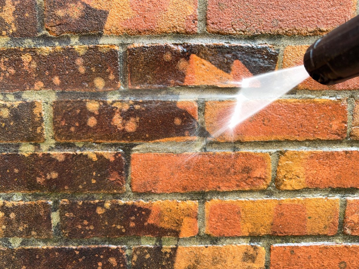 Close up of a pressure washer cleaning dirty bricks on a wall
