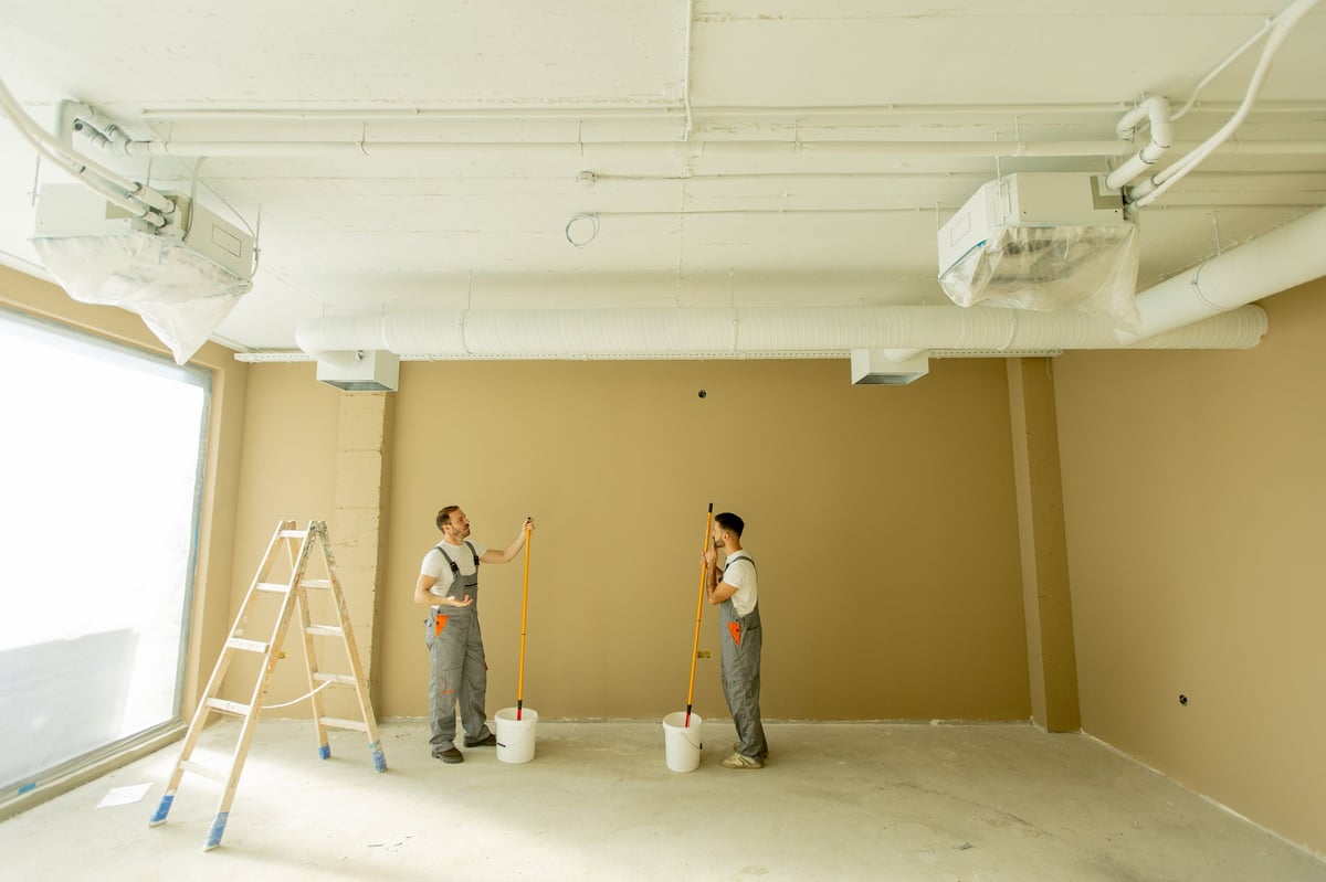 Two professional painters refreshing a wall in a bright, well-lit interior room