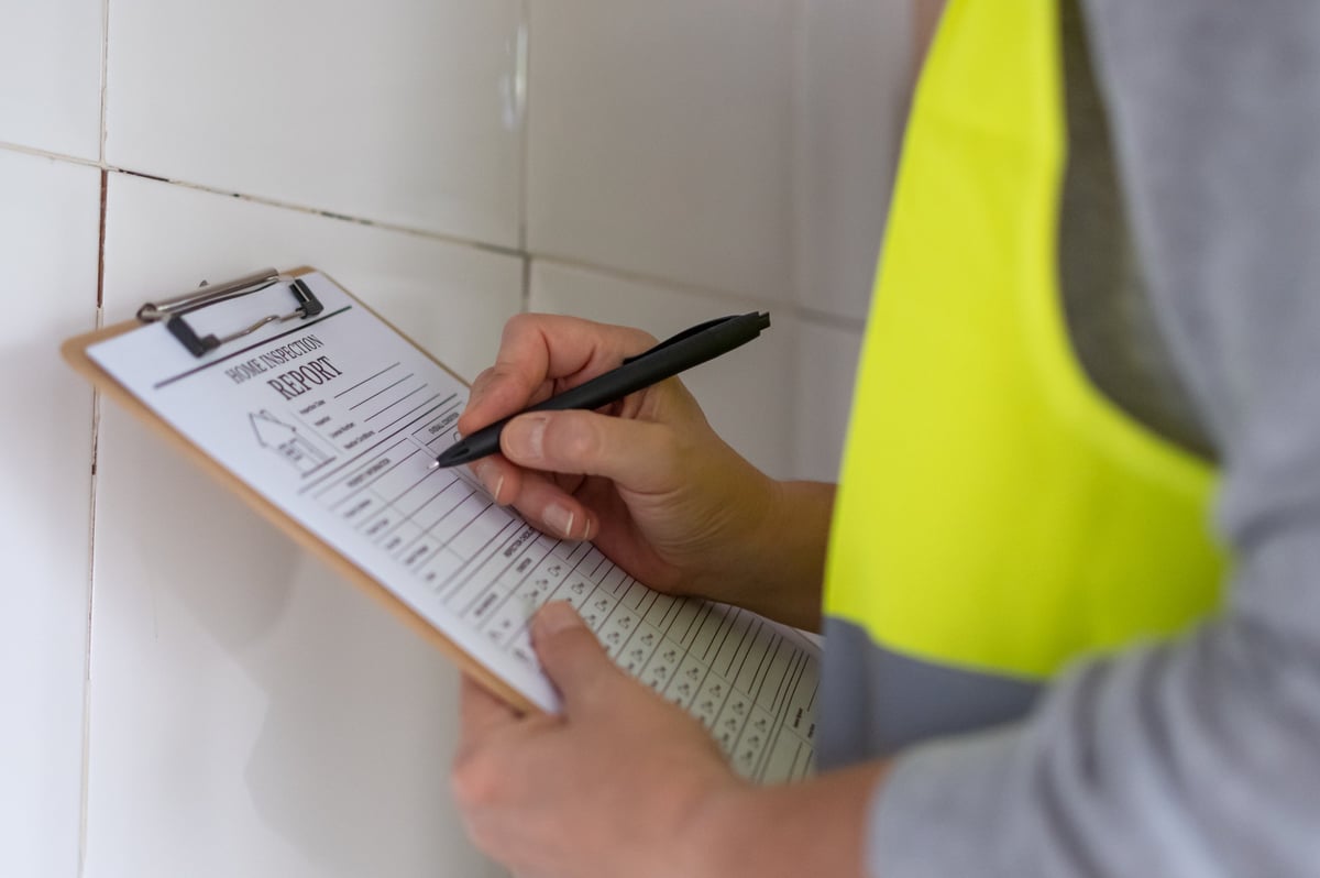 Property inspector in a safety vest holding a clipboard and checking an interior wall for damage and structural condition
